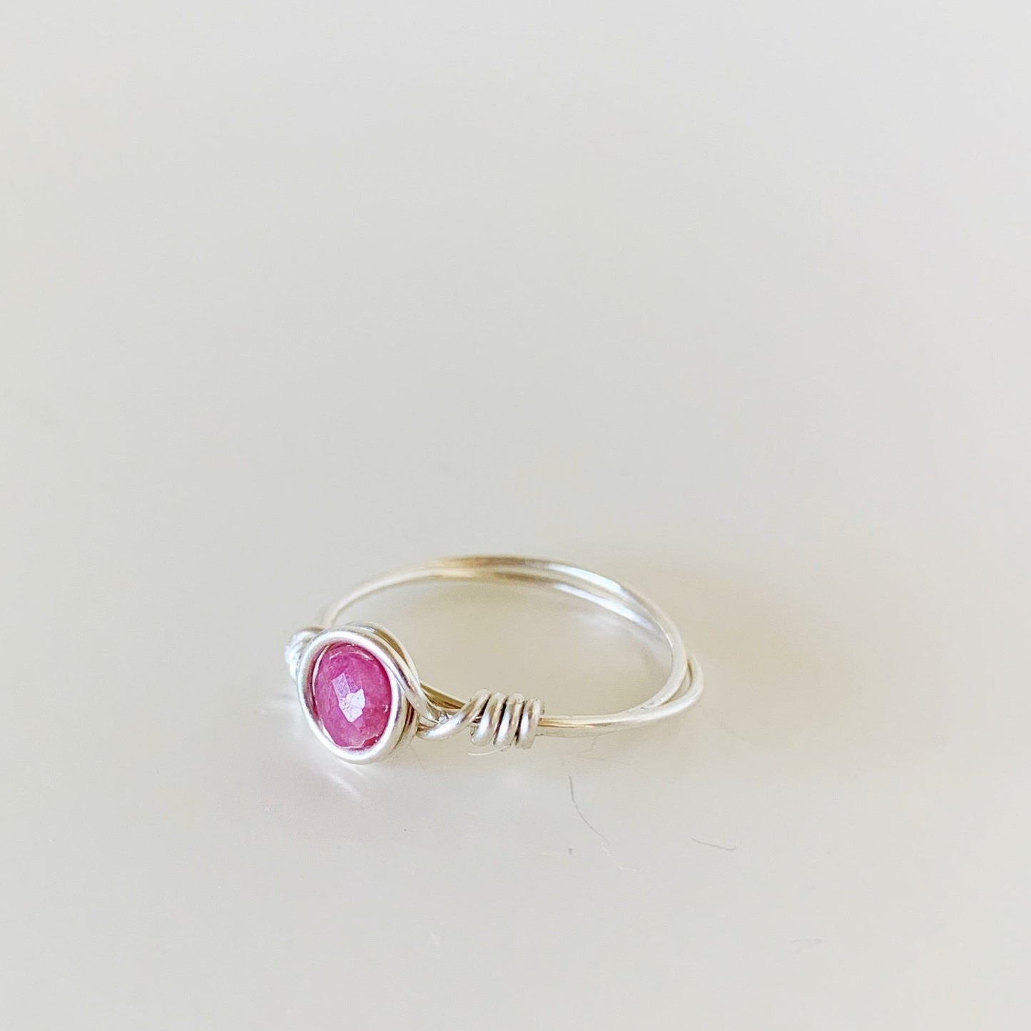 the harwich port ring by mermaids and madeleines is a wire wrapped ring created with sterling silver and has a pink tourmaline faceted coin bead at the center. this ring is facing to the left and photographed on a white surface