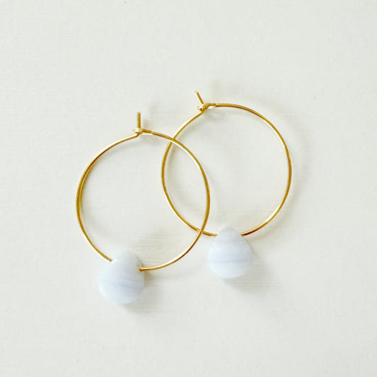Gold hoop earrings with small pastel purple bead drops, photographed on a plain off-white background.
