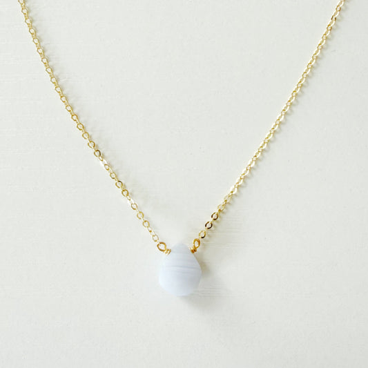 A delicate gold chain necklace with a small, smooth, pale blue-gray bead pendant, displayed against a clean, off-white background.
