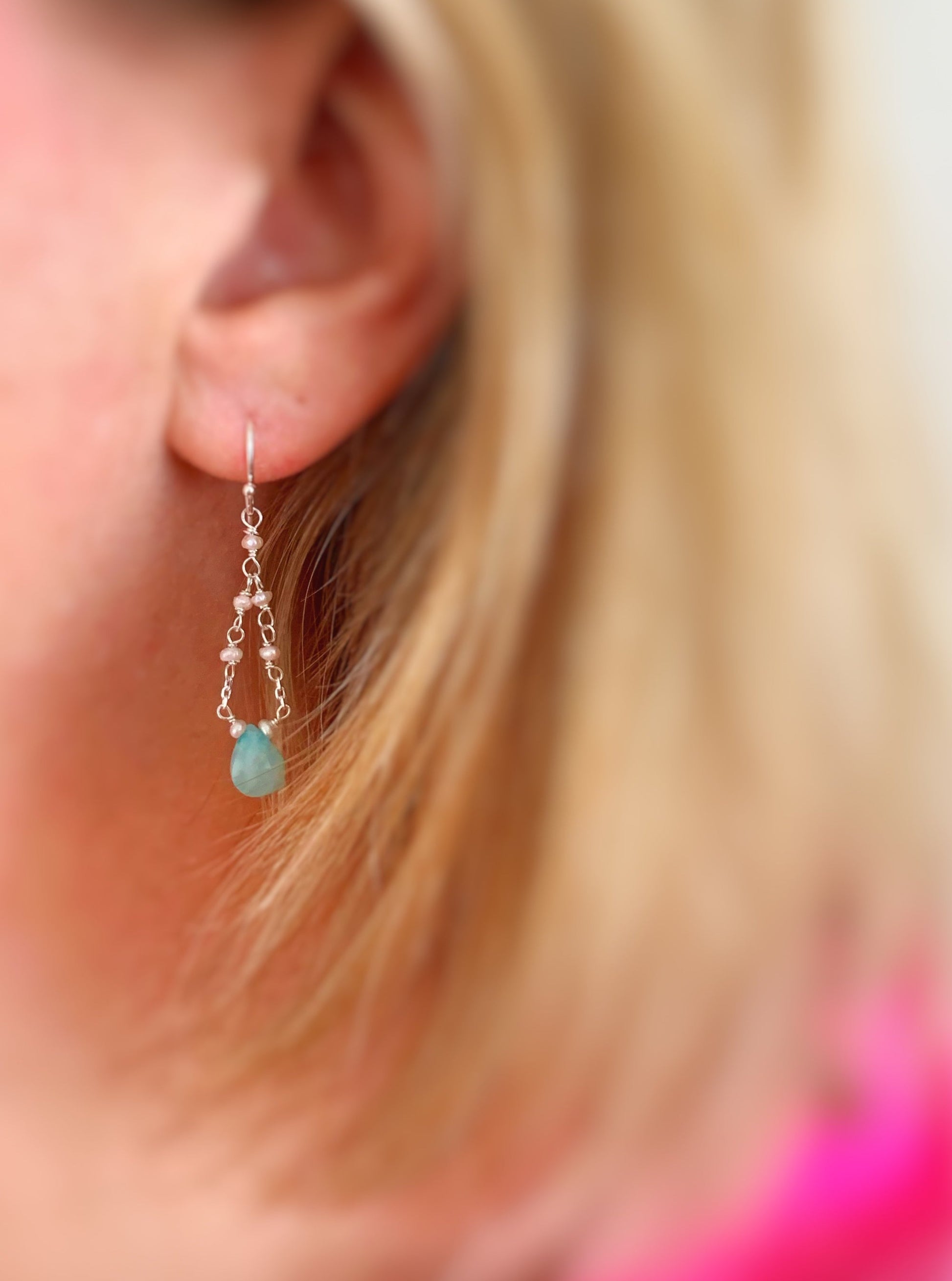 The island air earring by mermaids and madeleines in sterling silver has a amazonite teardrop at the center of the drop earring and then chain with freshwater pearls that loops to the top. this is a photo of a person wearing the earring with a close up view