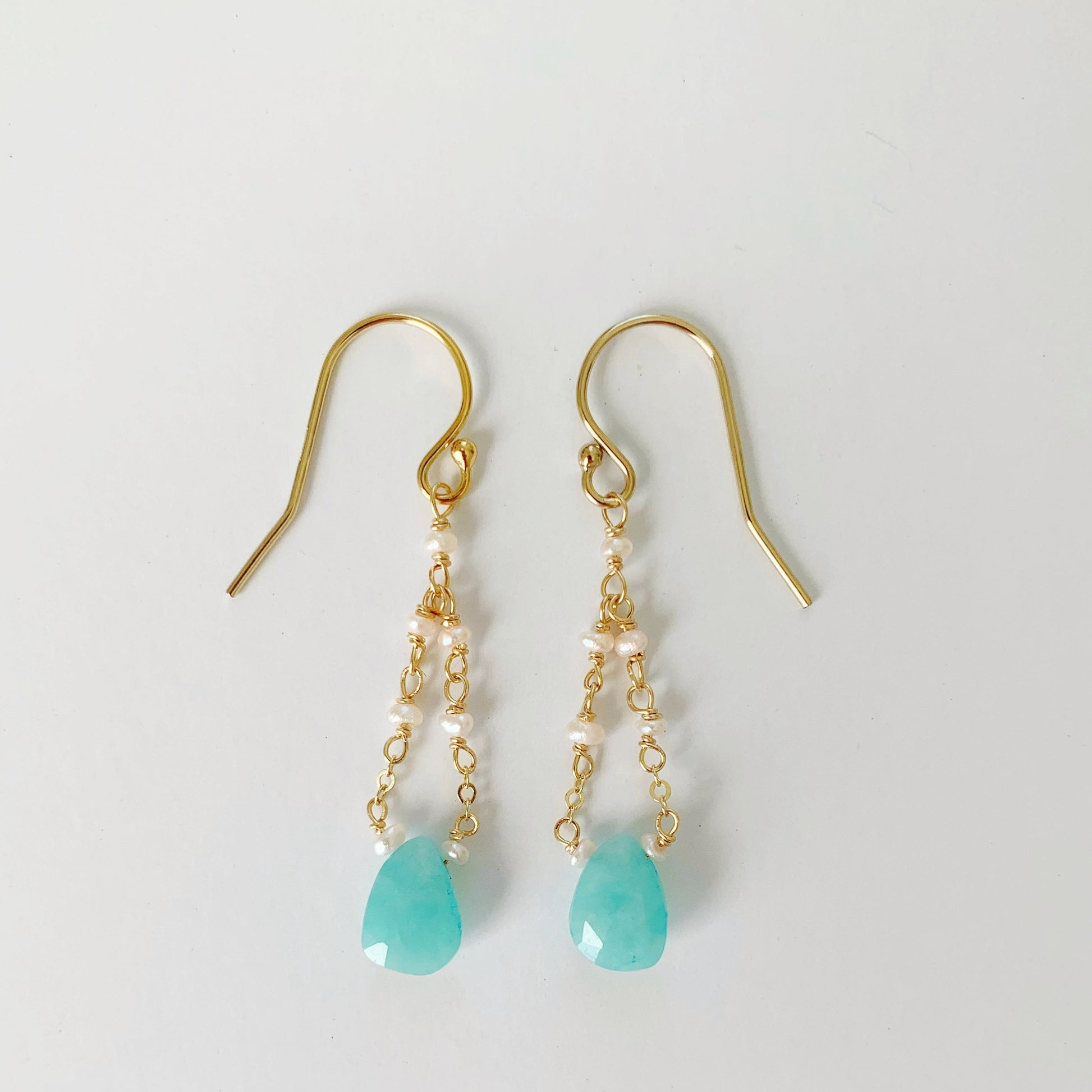 the island air earrings by mermaids and madeleines are created with amazonite teardrop shape stones at the bottom of the earring with a mix of 14k gold filled chain and pearls looping to the earring hook. this pair is photographed on a white background
