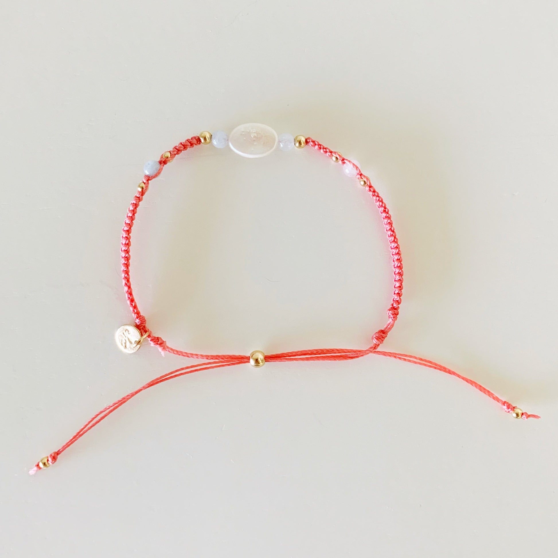 the kinda crabby bracelet by mermaids and madeleines is an adjustable macrame style bracelet designed with terra cotta color cord with a freshwater oval shaped pearl at the center with 4mm aquamarine beads on either side. this bracelet is photographed from the top down on a white surface