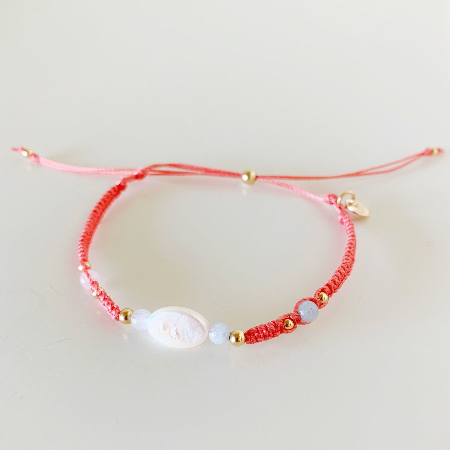 the kinda crabby bracelet by mermaids and madeleines is an adjustable macrame style bracelet created with terra cotta color cord with a freshwater oval pearl in the center with 4mm aquamarine beads on either side. this bracelet is photographed from the front on a white surface