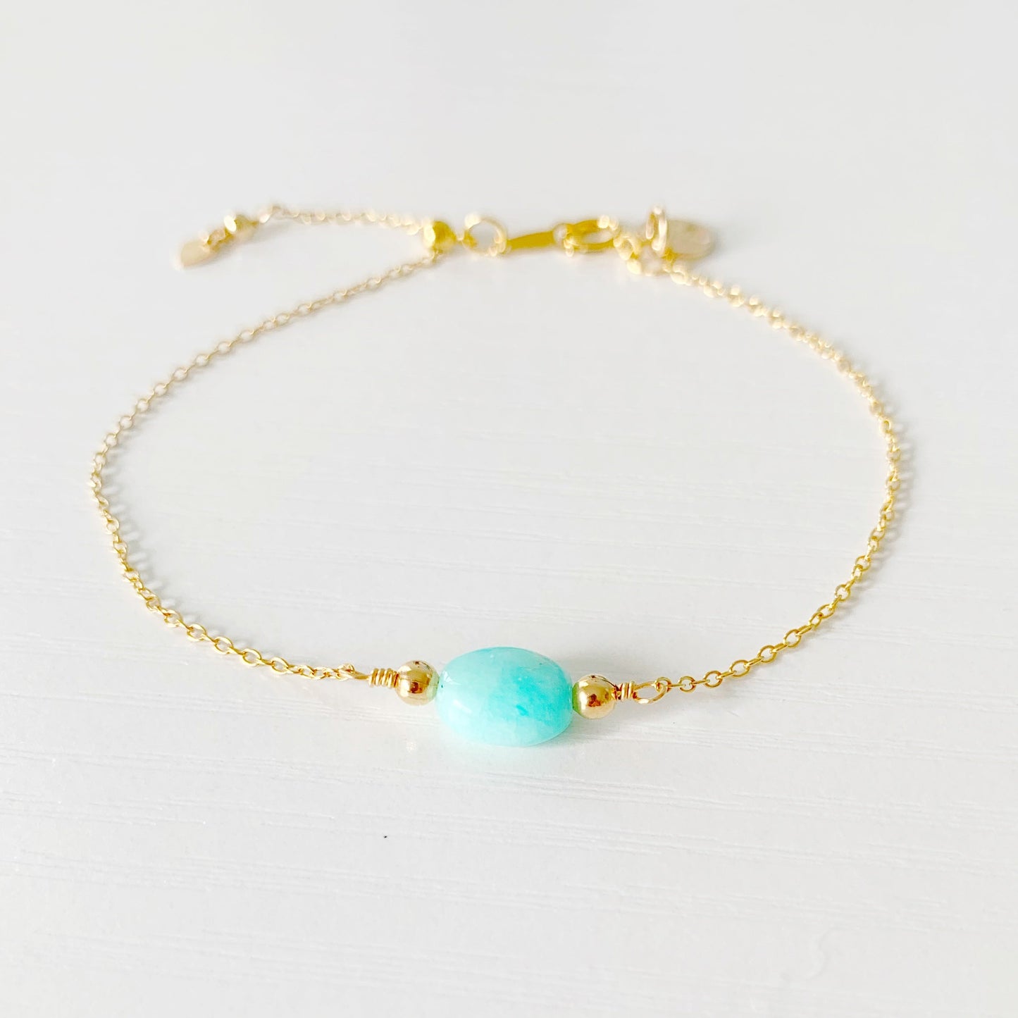 the mermaids and madeleines laguna bracelet is an adjustable bracelet that is 14k gold filled chain with a aqua, oval amazonite bead at the center. there's a slide bead near the clasp making the bracelet adjustable. this bracelet is photographed on a white surface