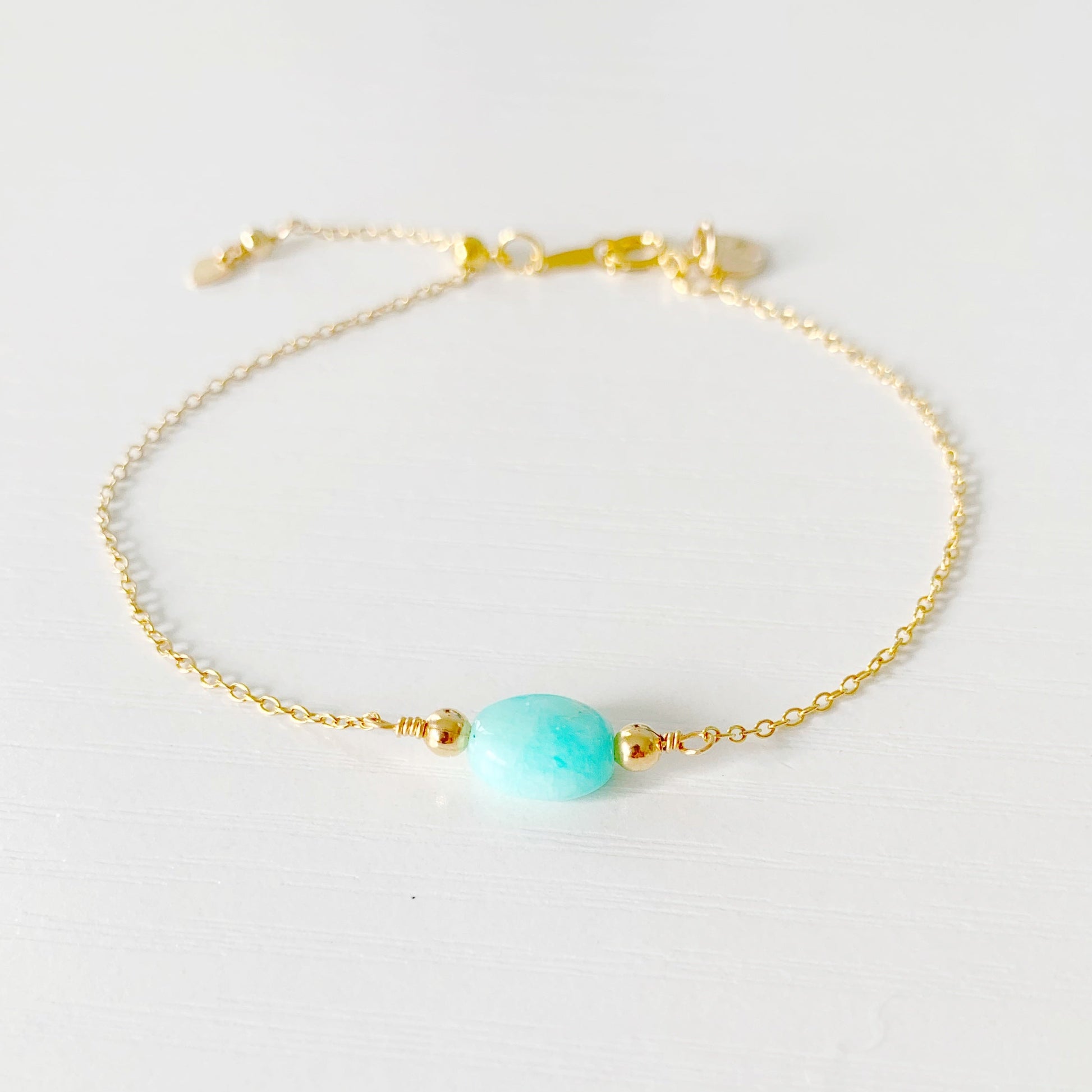 the mermaids and madeleines laguna bracelet is an adjustable bracelet that is 14k gold filled chain with a aqua, oval amazonite bead at the center. there's a slide bead near the clasp making the bracelet adjustable. this bracelet is photographed on a white surface