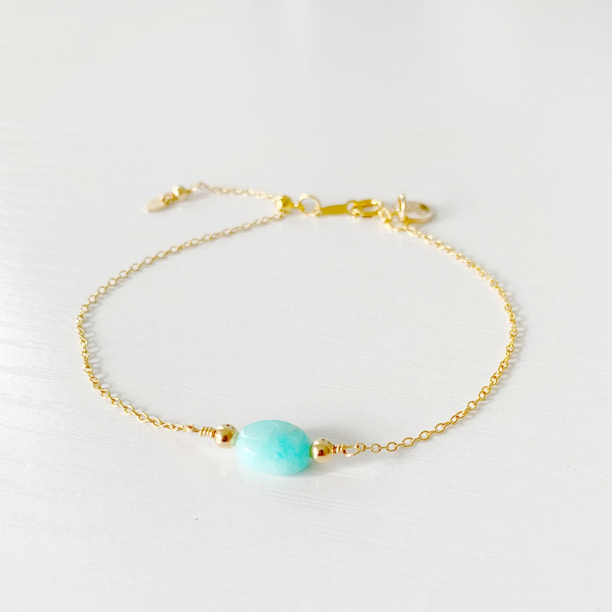 the laguna bracelet by mermaids and madeleines is a 14k gold filled chain style bracelet with an aqua oval amazonite at the center. There's a slide bead near the clasp that makes the bracelet adjustable. this bracelet is photographed from the front on a white surface