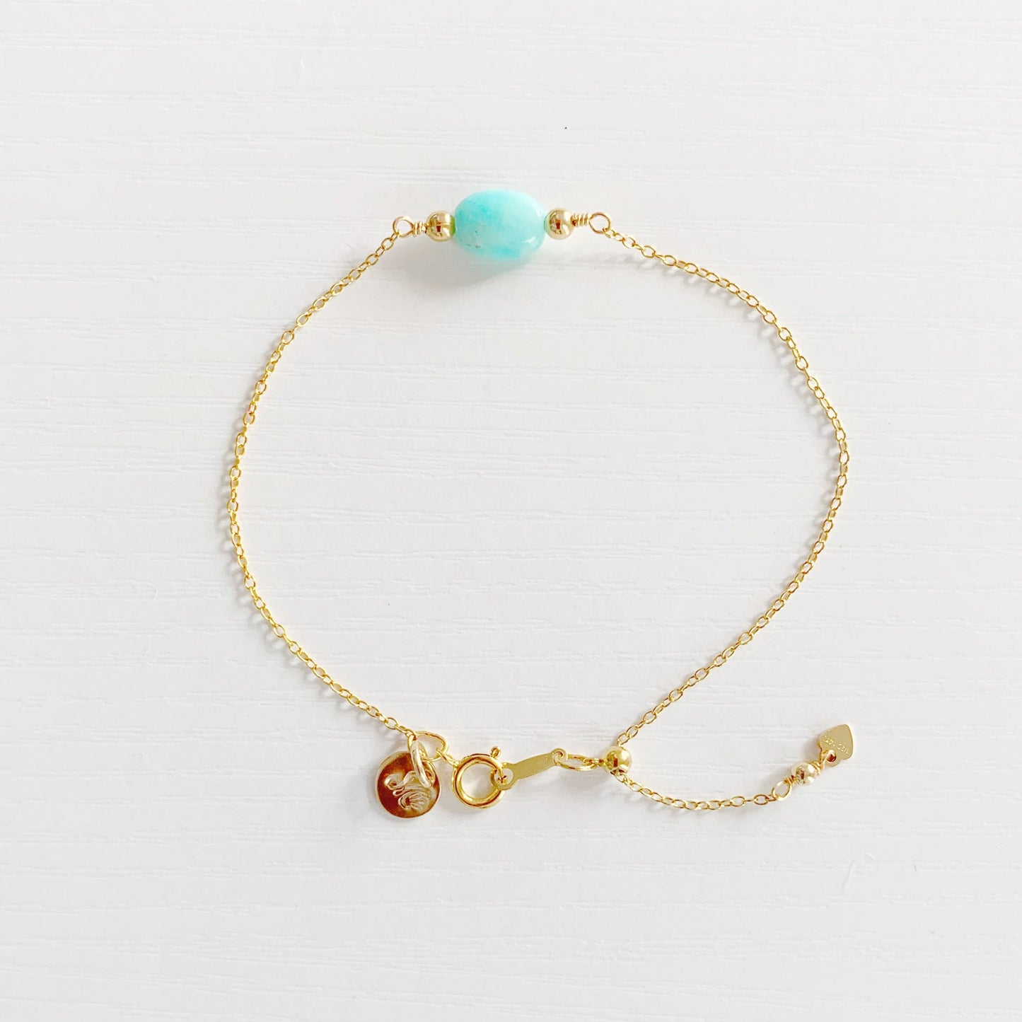the mermaids and madeleines laguna adjustable bracelet is created with 14k gold filled chain and an aqua oval amazonite at the center. the bracelet has a slide bead near the clasp making it adjustable. this bracelet is photographed on a white surface from the top down.