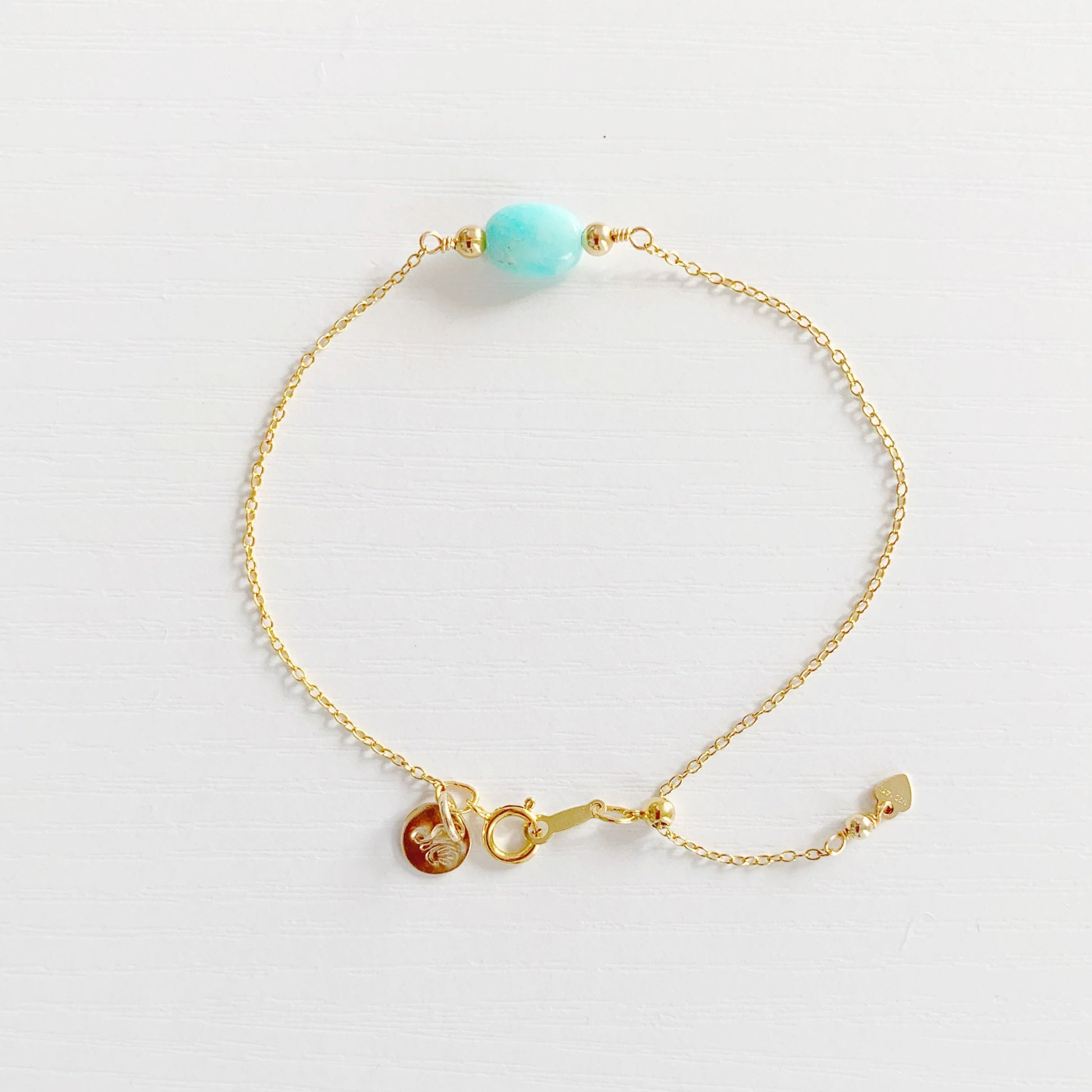 the mermaids and madeleines laguna adjustable bracelet is created with 14k gold filled chain and an aqua oval amazonite at the center. the bracelet has a slide bead near the clasp making it adjustable. this bracelet is photographed on a white surface from the top down.