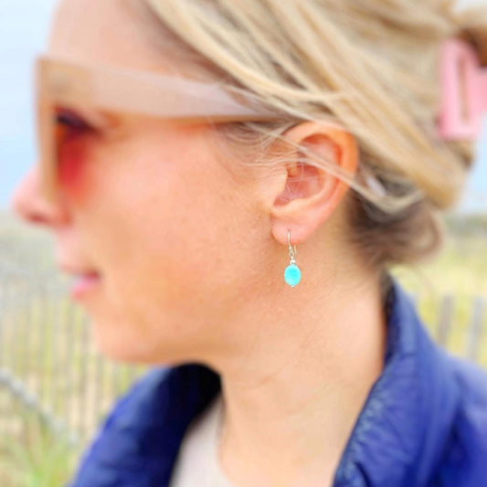 the mermaids and madeleines laguna earrings are simple drop style earrings created with smooth, aqua, oval amazonite beads dropped from sterling silver findings and ear wires. this pair of earrings is photographed on an earlobe 
