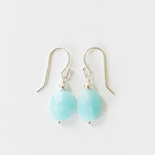 the laguna earrings by mermaids and madeleines are simple drop earrings with faceted oval amazonite beads hanging from sterling silver earring findings. this pair is photographed on a white surface