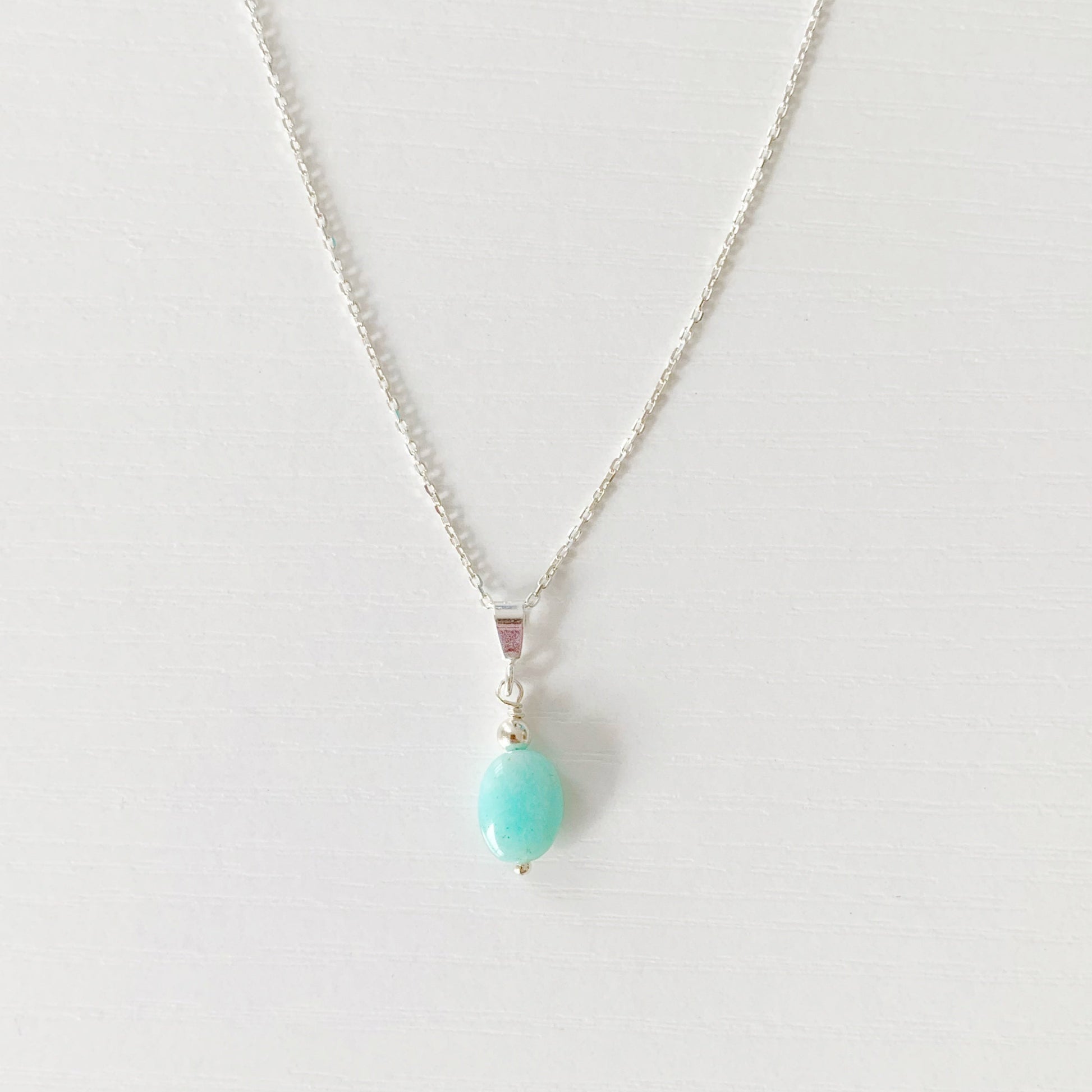 the laguna necklace by mermaids and madeleines is a pendant style necklace with a smooth, oval, amazonite bead with sterling silver findings and chain. this necklace is photographed on a white surface