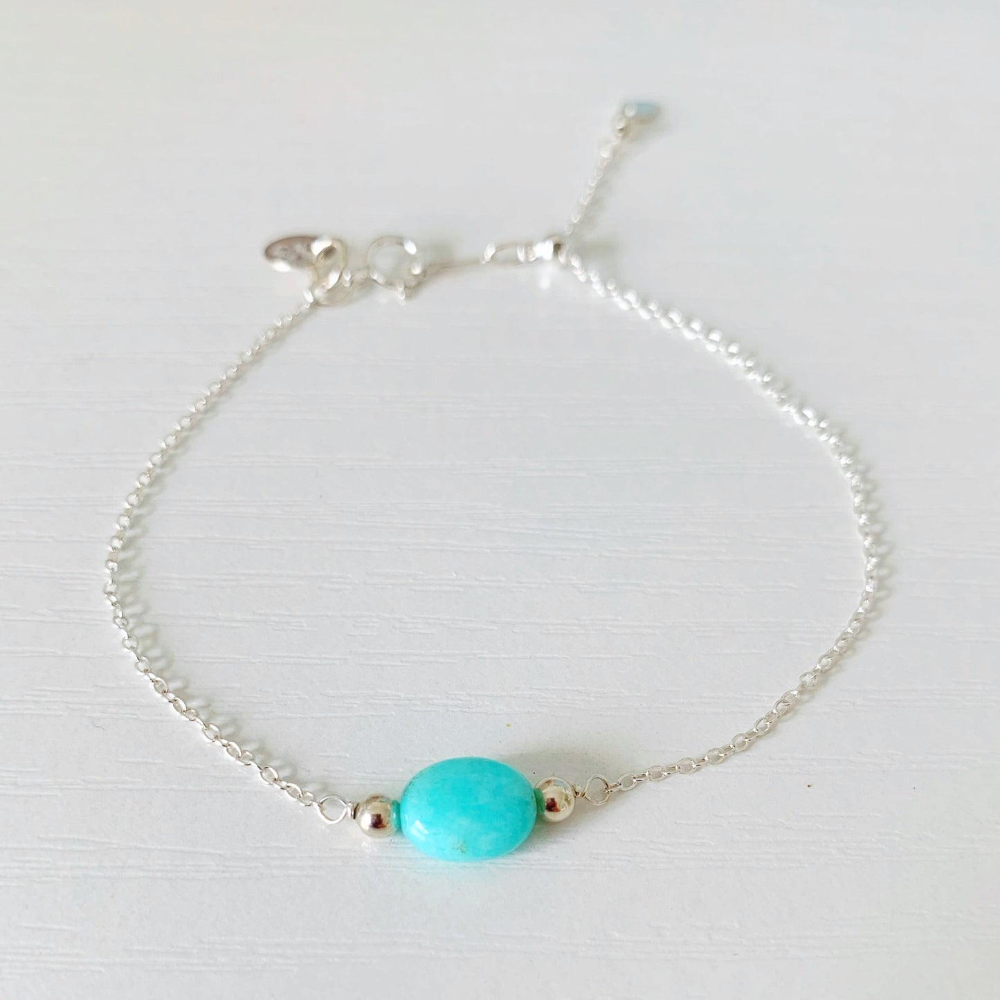 the laguna bracelet is created on sterling silver chain with an adjustable slide clasp and an oval amazonite bead at the center. this bracelet is pictured on a white surface