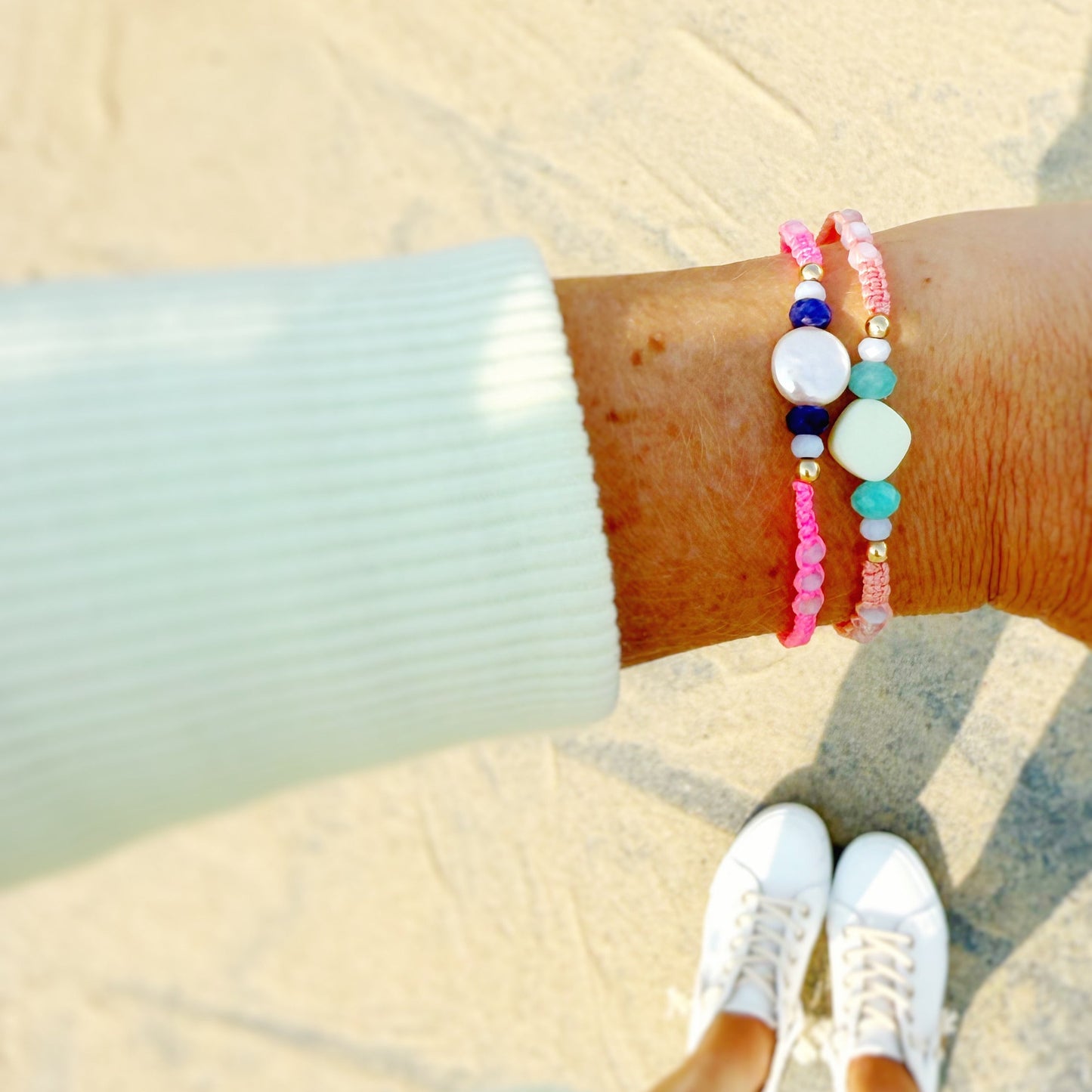 Person wearing colorful woven and beaded bracelets on a sandy beach.