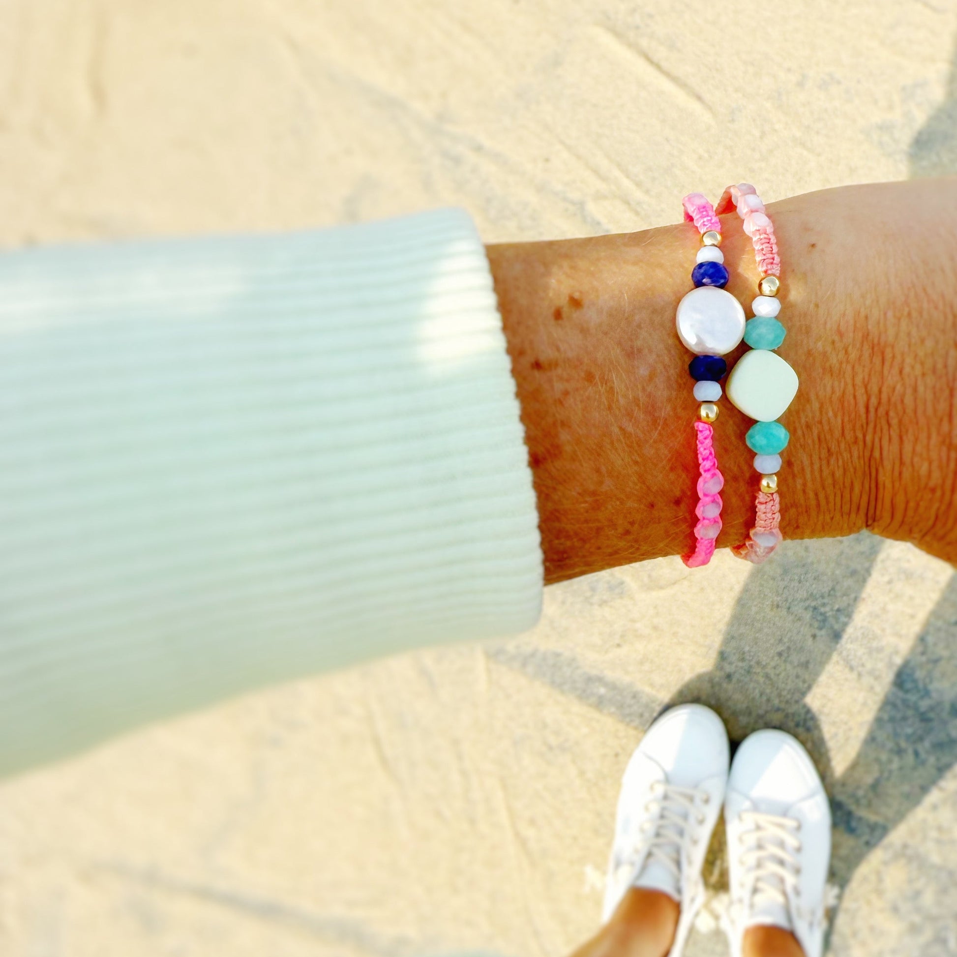 Person wearing colorful woven and beaded bracelets on a sandy beach.
