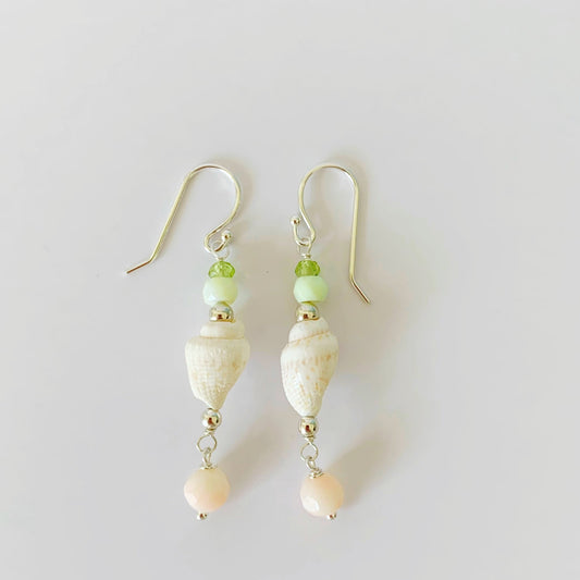 the margarita shellebration earrings by mermaids and madeleines are a linear drop earring featuring a shell at the center complimented by peridot, green opal and a coral drop bead all with sterling silver findings. this pair is photographed on a white surface.
