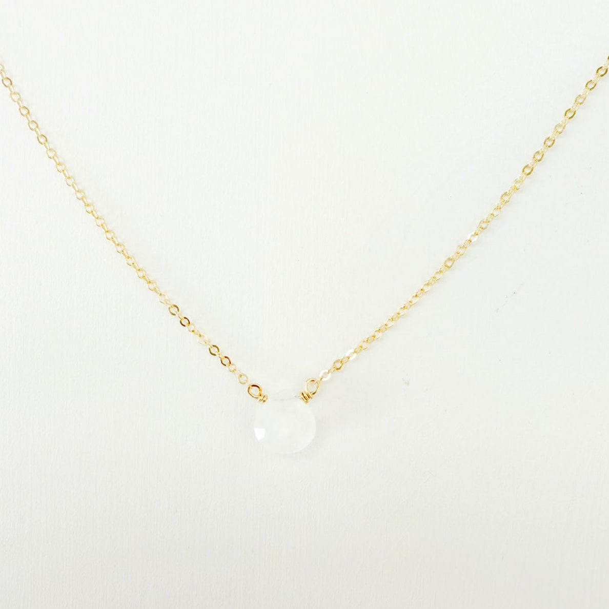 the marshmallow necklace by mermaids and madeleines is a dainty 14k gold filled chain necklace with a tiny moonstone drop at the center. this necklace is photographed close up on a white surface