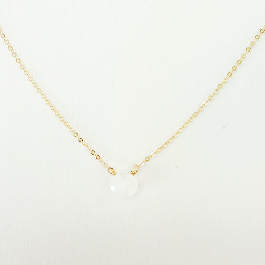 the marshmallow necklace by mermaids and madeleines is a dainty 14k gold filled chain necklace with a tiny moonstone drop at the center. this necklace is photographed close up on a white surface
