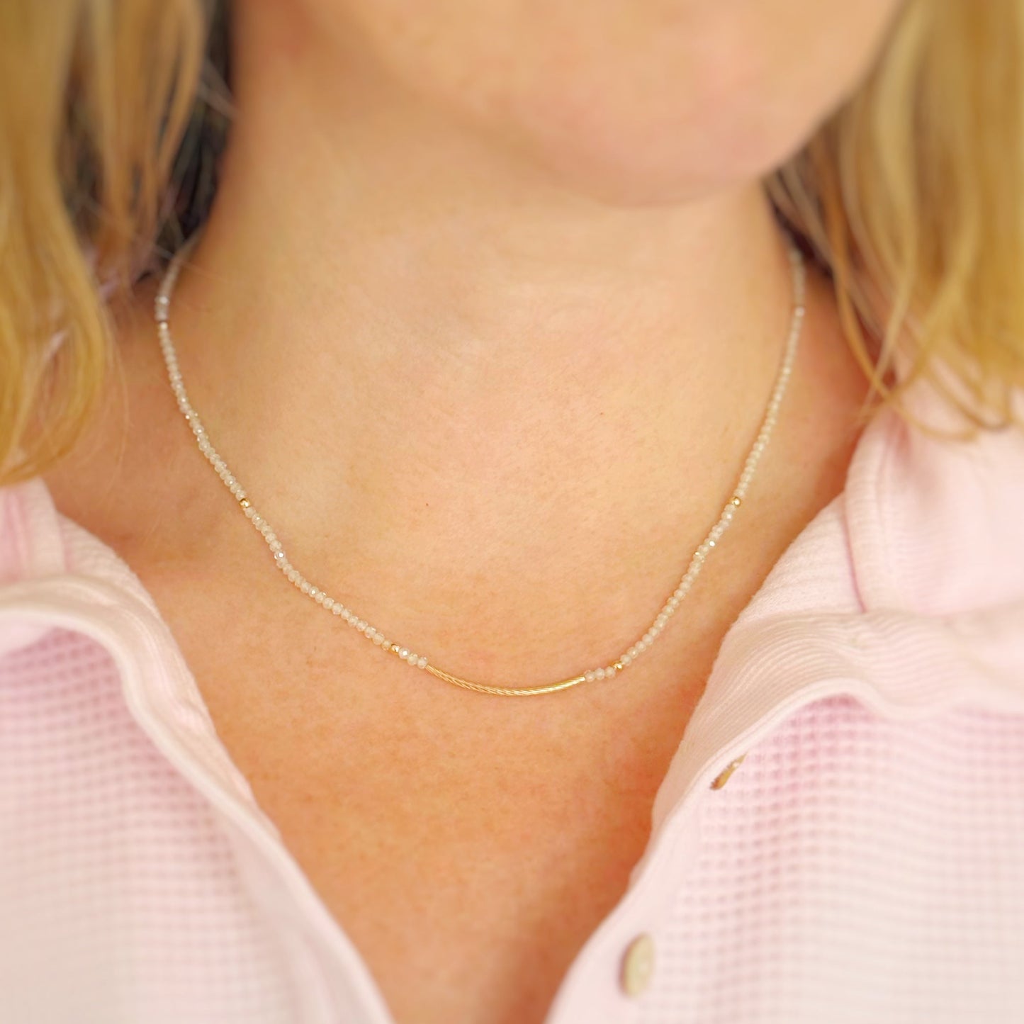 Close-up of a person wearing a delicate beaded and gold necklace with a pink shirt.