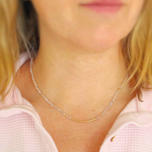 Close-up of a person wearing a delicate pastel beaded gold bead necklace with a blurred background