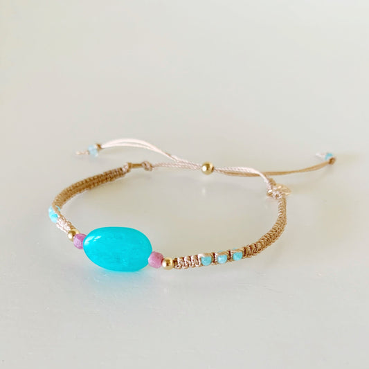the harwich port adjustable macrame bracelet by mermaids and madeleines in color moonlit beach is a friendship style bracelet with a slide bead clasp. the bracelet features a large amazonite bead at the center with smaller amazonite rondelles on the sides and its complimented by pink tourmaline and 14k gold filled beads. this bracelet is facing slightly to the left and photographed on a white surface