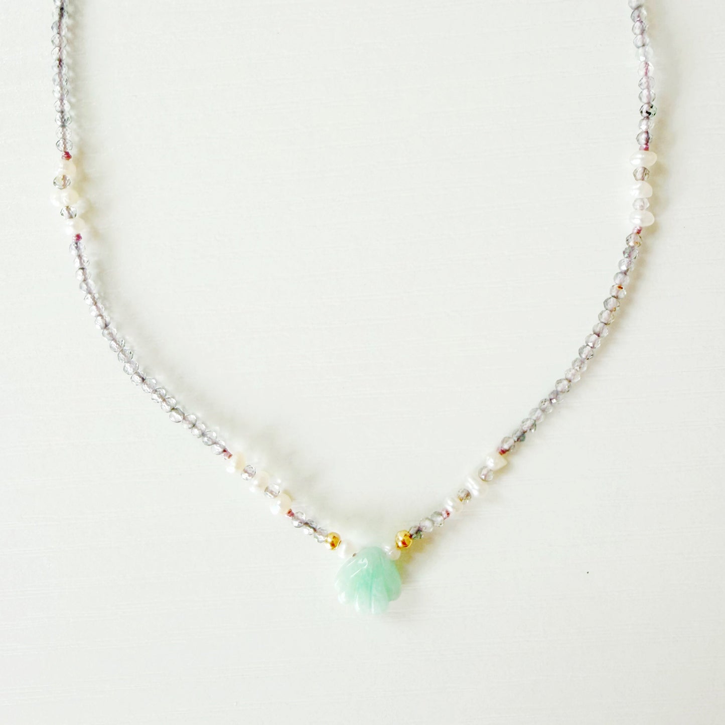 Necklace with small beads and a central green gemstone shell on a white background