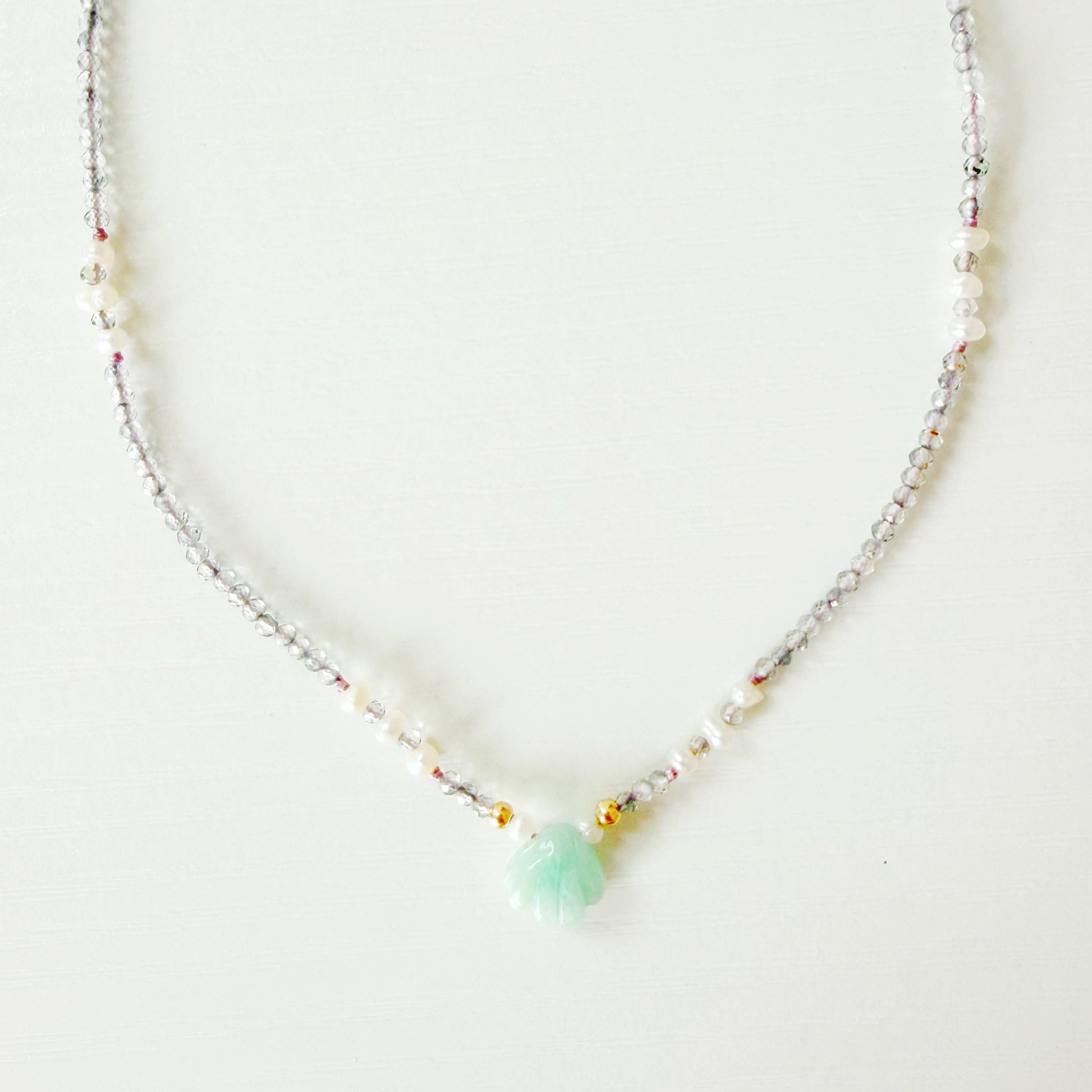 Necklace with small beads and a central green gemstone shell on a white background