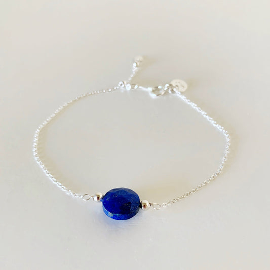 the neptune adjustable bracelet in sterling silver by mermaids and madeleines is a chain based bracelet with a slide bead near the clasp. the bracelet has a royal blue faceted coin lapis bead at the center and is photographed flat on a white surface