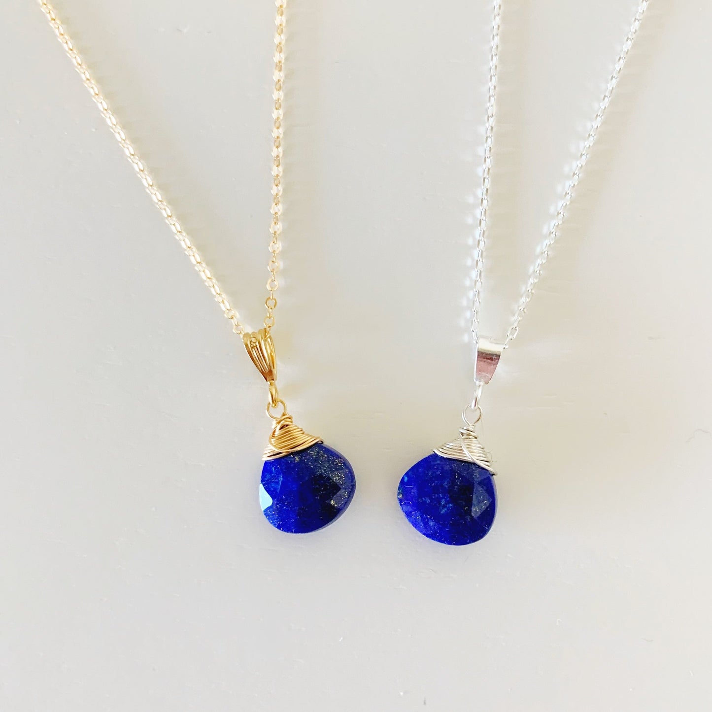 Neptune pendant necklace by mermaids and madeleines with blue lapis briolette is wire wrapped  available sterling silver or 14k gold filled. Photographed here are 2 neptune pendants one in sterling silver and one 14k gold filled pictured on a white background.