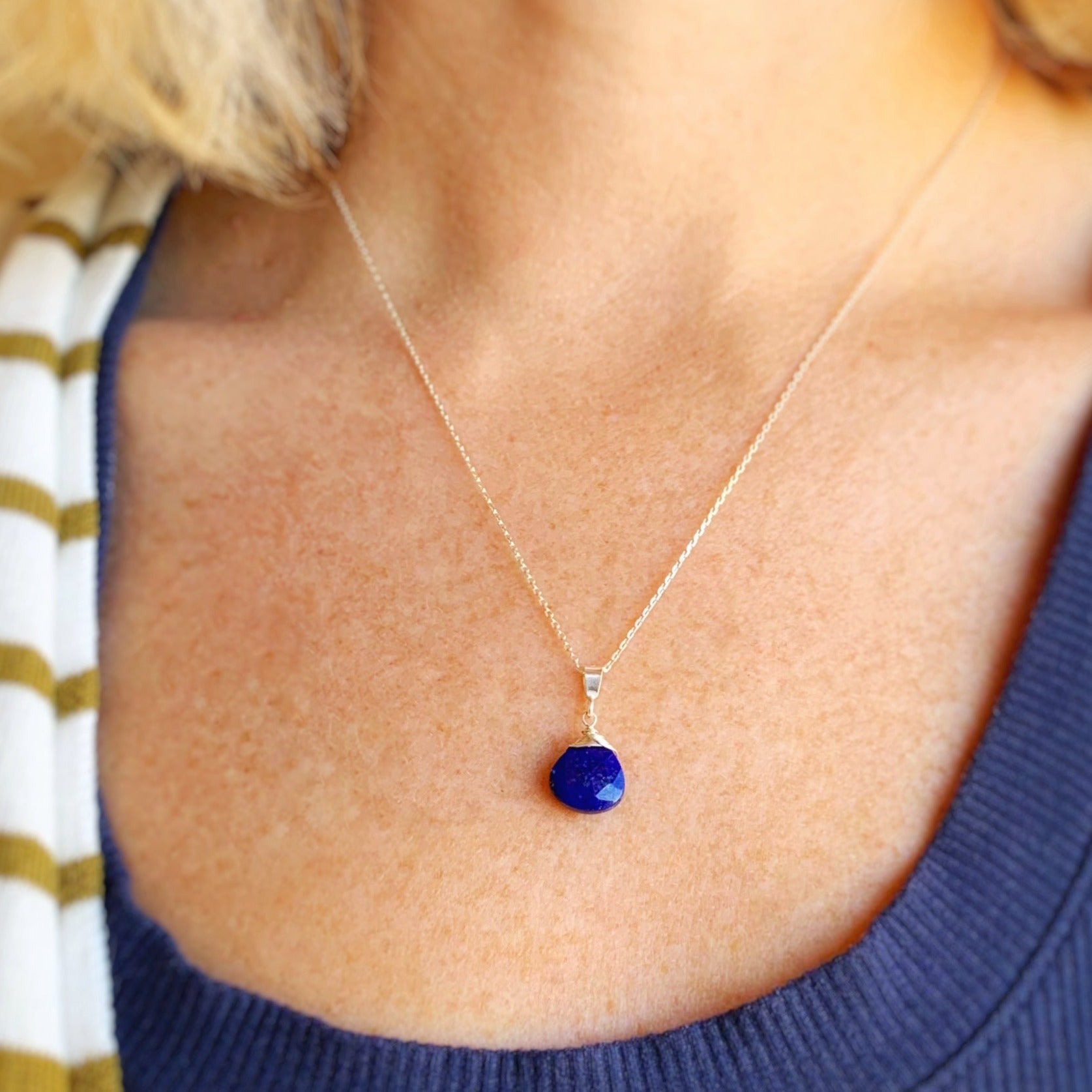 the neptune pendant necklace by mermaids and madeleines features a sterling silver wire wrapped royal blue lapis briolette as a pendant with sterling silver findings and chain. this necklace is photographed worn on a person with a close up view with a little bit of sweater in view