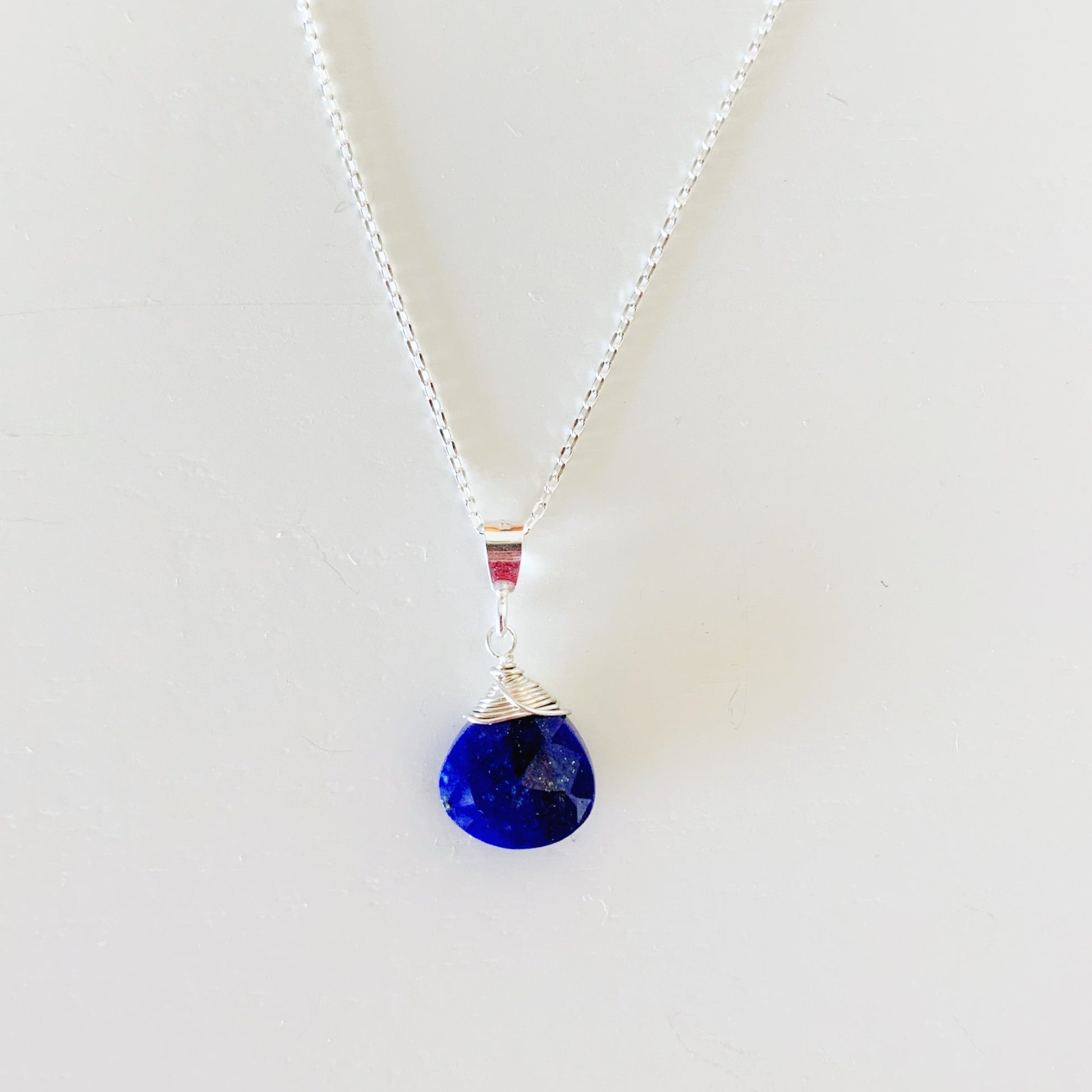 The neptune pendant necklace by mermaids and madeleines is created with a blue lapis faceted briolette, wrapped in sterling silver wire on a sterling silver chain. this necklace is photographed on a white background