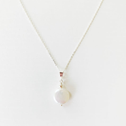 the newport necklace by mermaids and madeleines is a freshwater coin pearl suspended from a sterling silver chain and findings. this necklace is photographed on a white surface