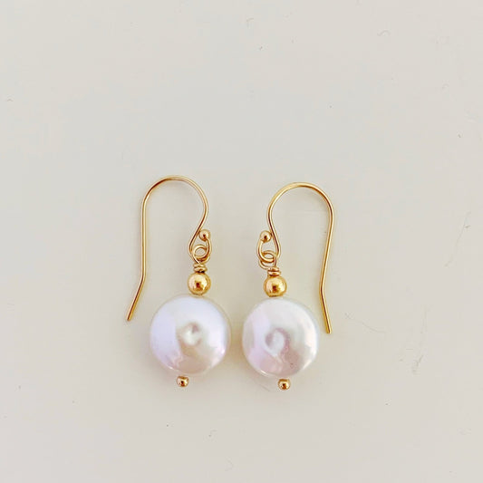 the newport earrings by mermaids and madeleines are a classic style earring designed with white, freshwater coin pearls and 14k gold filled beads and findings. this pair is photographed flat on a white surface