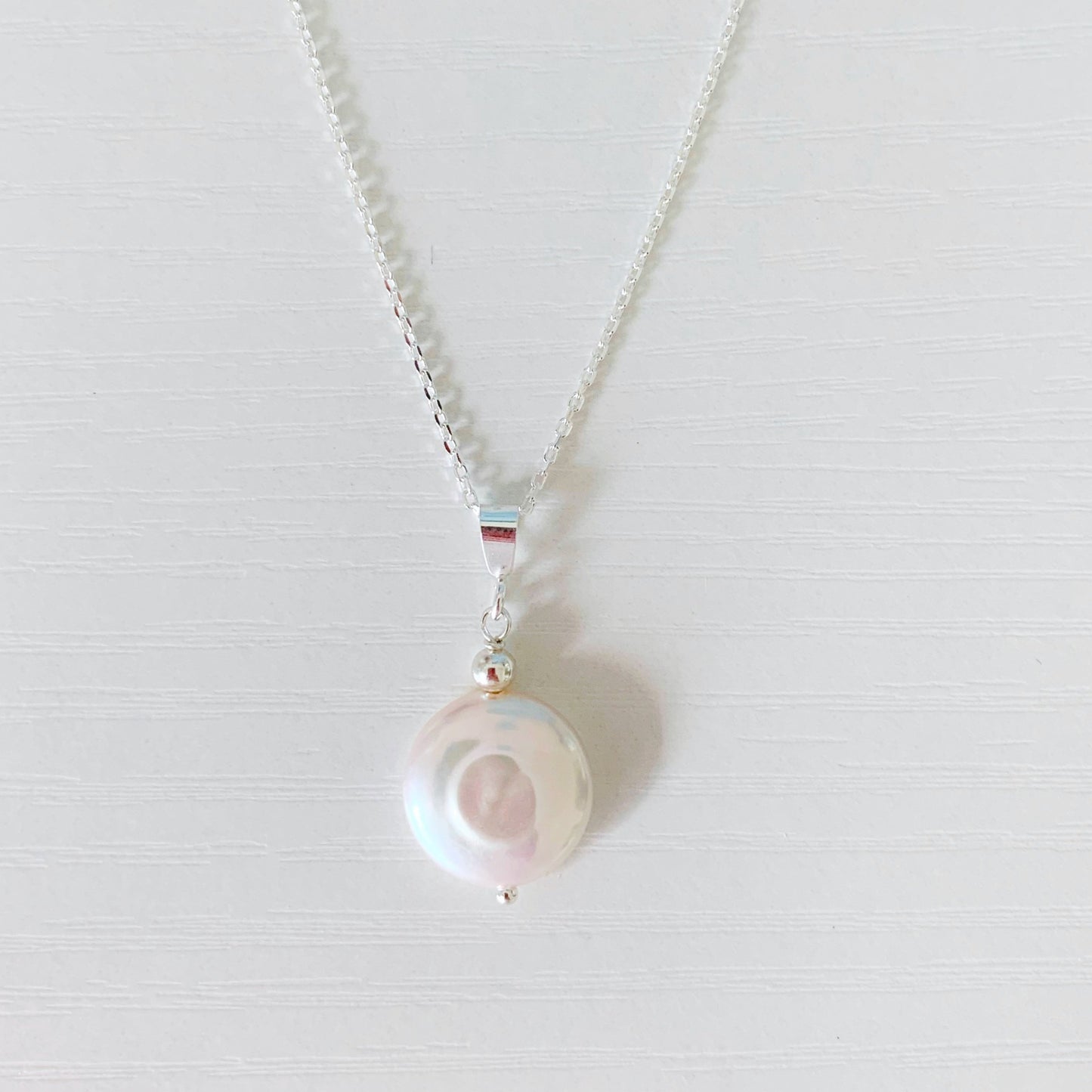 the newport gala necklace is created with a large freshwater coin pearl suspended from dainty sterling silver chain. this necklace is photographed on a white surface