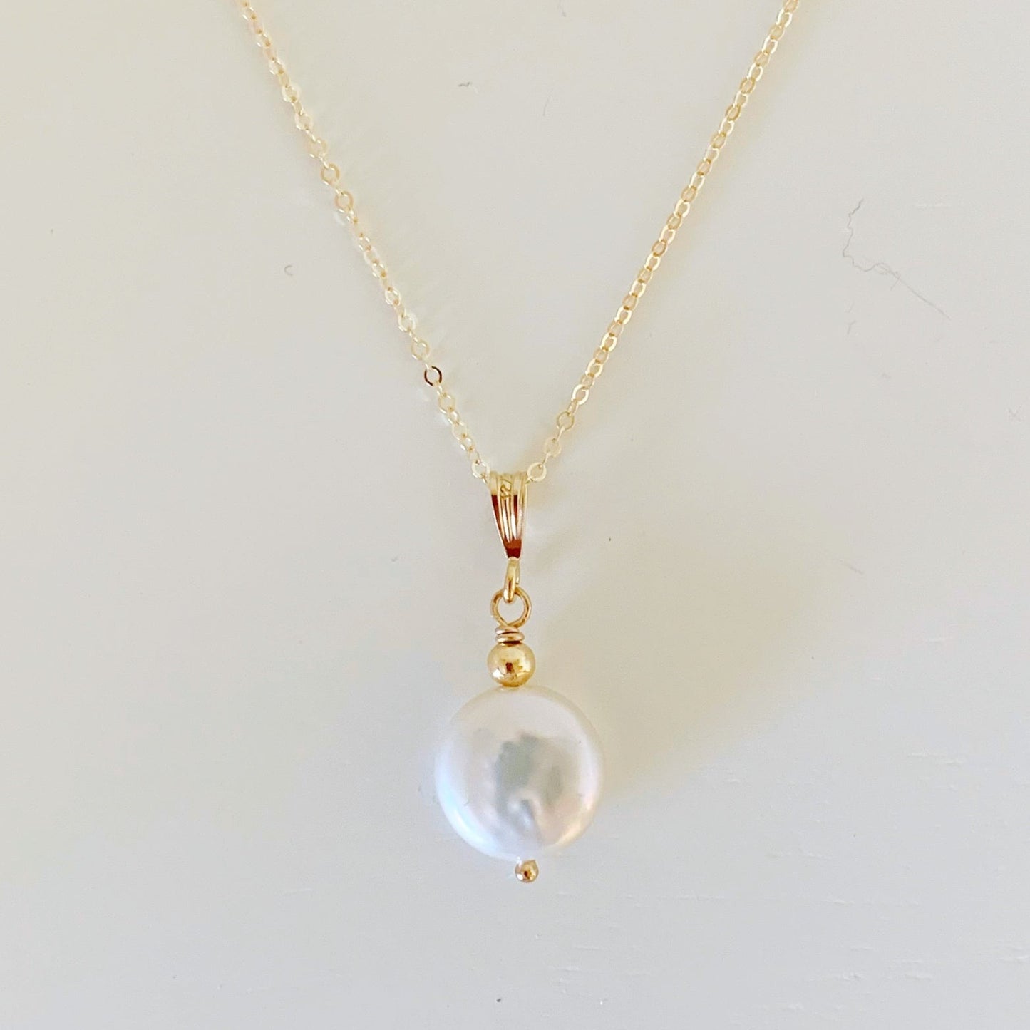 the newport pendant by mermaids and madeleines is a simple style designed with a white freshwater coin pearl with 14k gold filled chain and findings. this necklace is photographed flat on a white surface