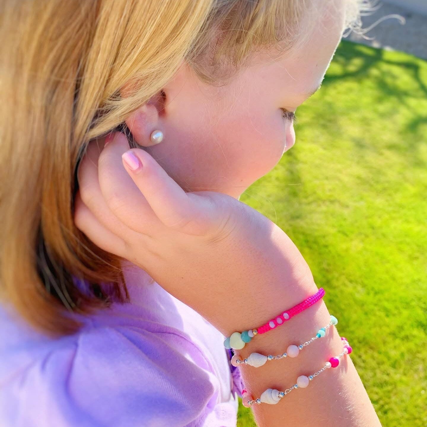 Child wearing multiple bracelets on a grassy background