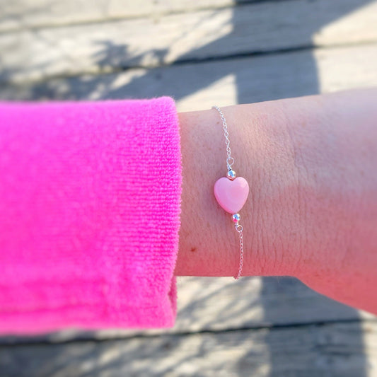 Hand wearing a pink heart-shaped bracelet over a wooden boardwalk surface