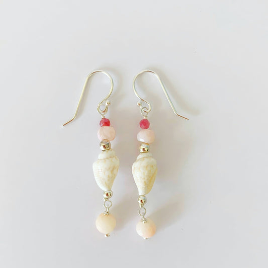 the pink lemonade shellebration earrings by mermaids and madeleines are a linear drop earring featuring a shell at the center complimented by pink opal, tourmaline and a coral drop bead all with sterling silver findings. this pair is photographed on a white surface.