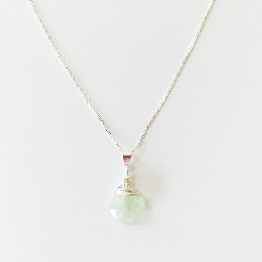 the raindrop necklace by mermaids and madeleines is a faceted briolette of aquamarine wire wrapped with sterling silver and hanging from a sterling silver chain with findings. this image is the front part of the necklace photographed on a white surface