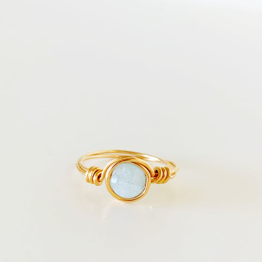 the raindrop ring by mermaids and madeleines is a wire wrapped ring created with 14k gold filled wire and features a faceted aquamarine coin bead at the center. this ring is photographed straight on and on a white surface