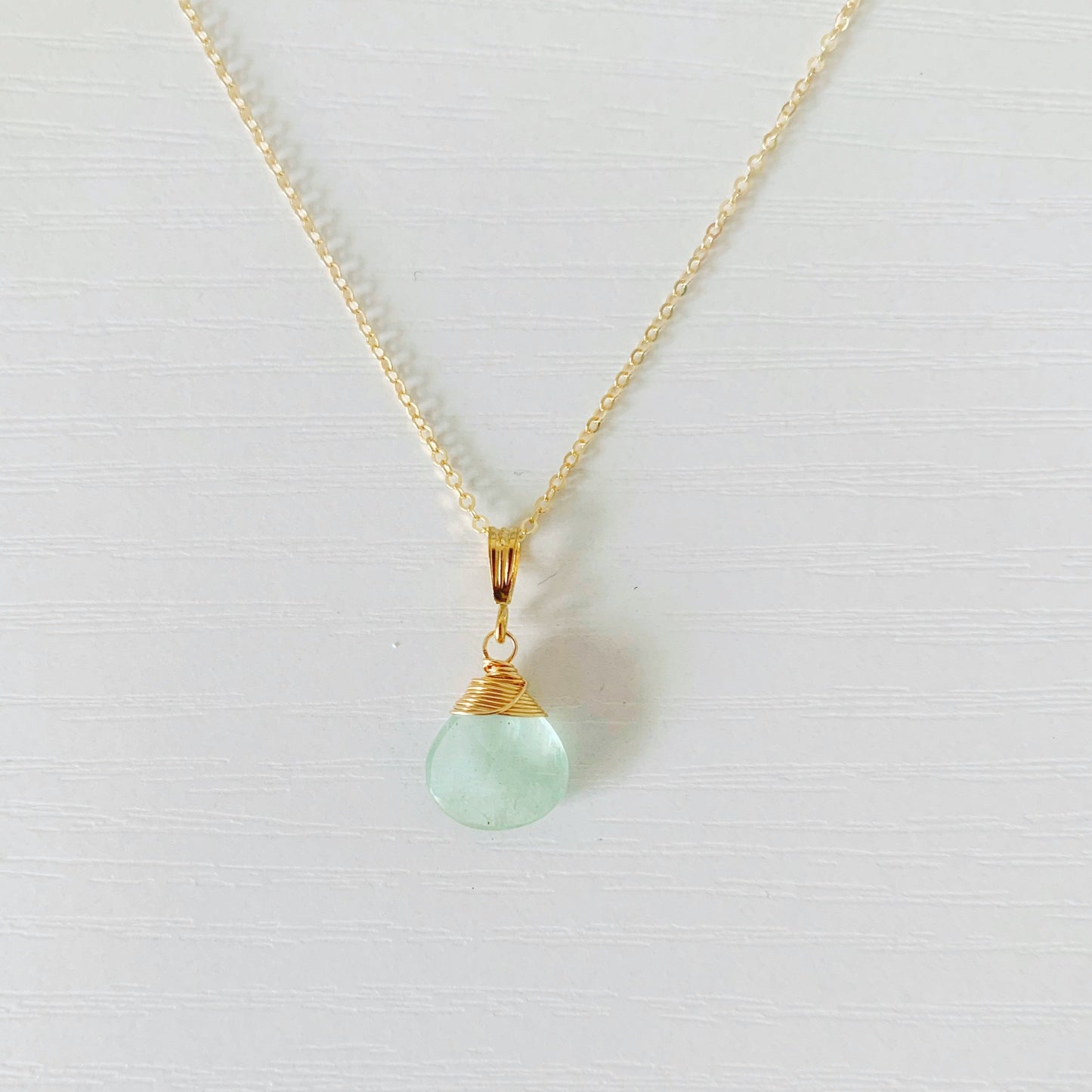14k gold filled wire wrapped aquamarine briolette suspended from a thin cable chain necklace. this is pictured over a white background