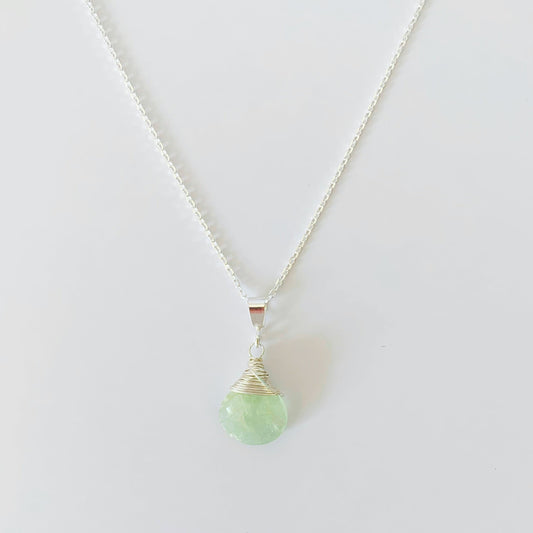 a wire wrapped aquamarine briolette with sterling silver suspended from a thin cable chain necklace. this picture is over a white surface