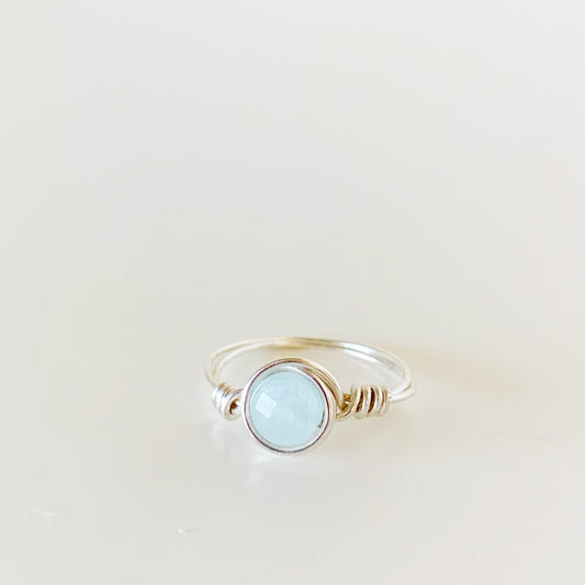 the raindrop ring by mermaids and madeleines is a sterling silver wire wrapped ring that features a faceted aquamarine coin bead in the center. this ring is photographed straight on and on a white surface