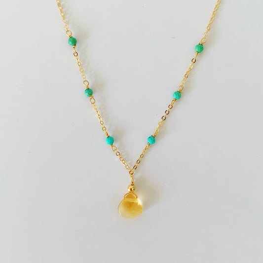 ray of sunshine necklace has a citrine drop at the center and natural turquoise beads on 14k gold filled chain. this necklace is photographed over a white surface