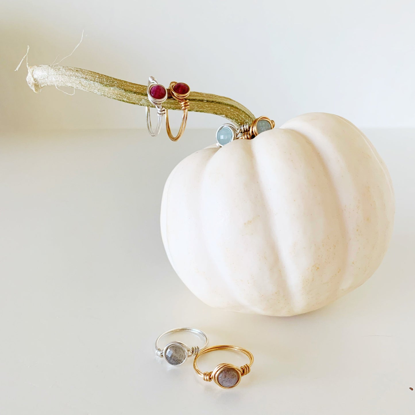 a variety of different mermaids and madeleines wire-wrapped rings are placed on and near a white pumpkin and photographed on a white surface