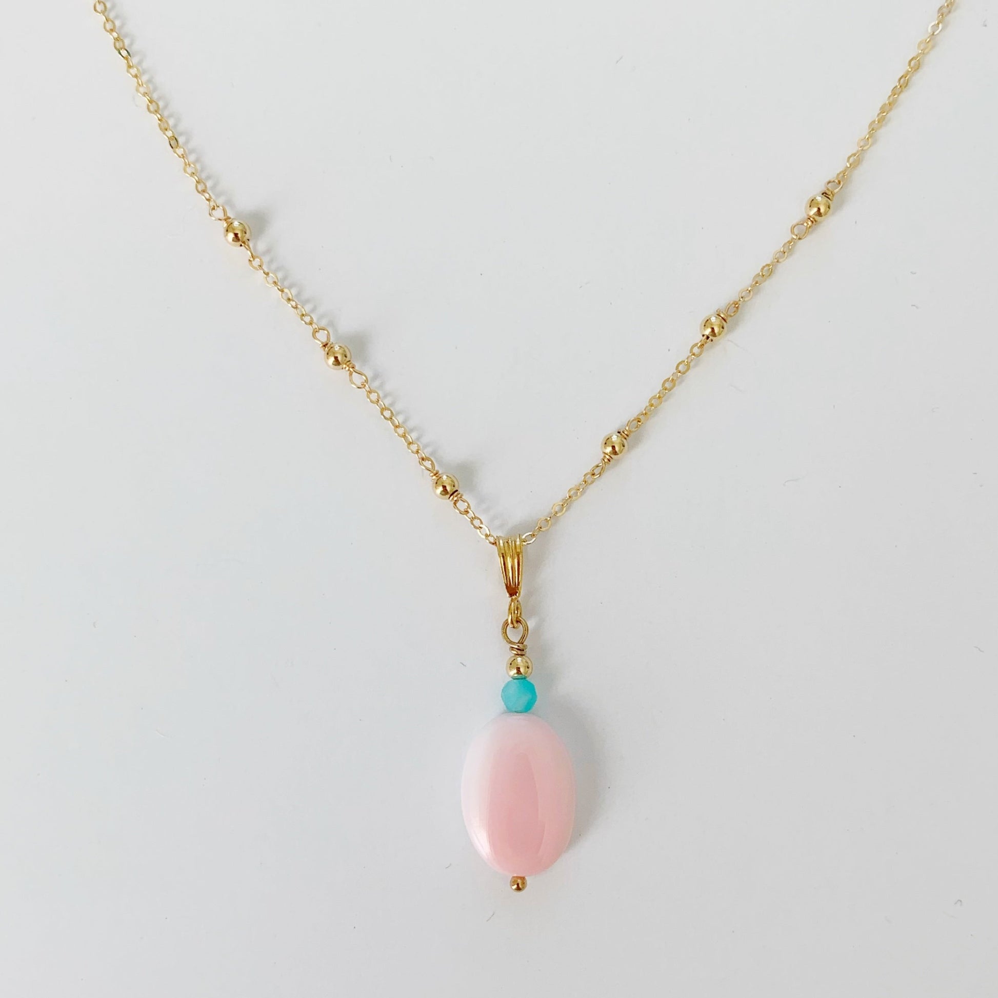 the sanibel necklace by mermaids and madeleines is created with an oval pink conch shell bead and amazonite bead to compliment suspended on a 14k gold filled dainty chain. this necklace is photographed on a white surface