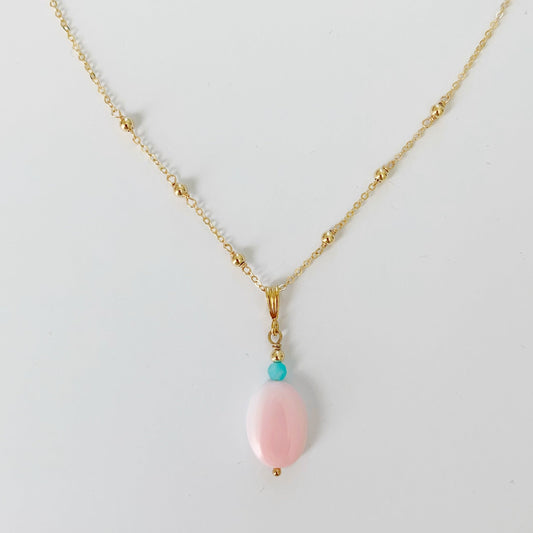 the sanibel necklace by mermaids and madeleines is created with an oval pink conch shell bead and amazonite bead to compliment suspended on a 14k gold filled dainty chain. this necklace is photographed on a white surface