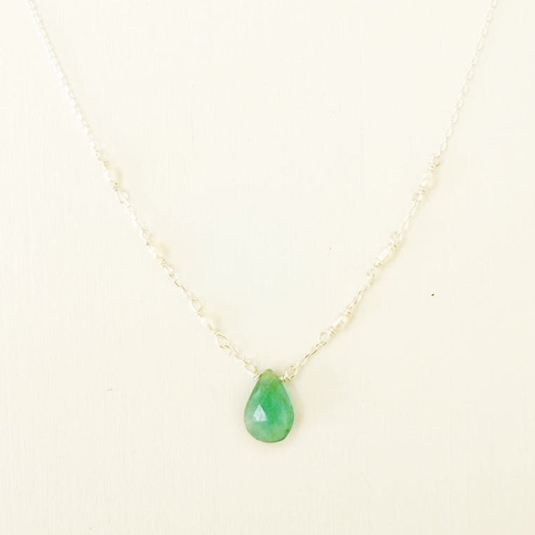 the sea salt necklace by mermaids and madeleines is a pendant style necklace with a teal grandidierite briolette at the center and tiny seed pearls on each side of the sterling chain. this necklace is photographed close up on a white surface