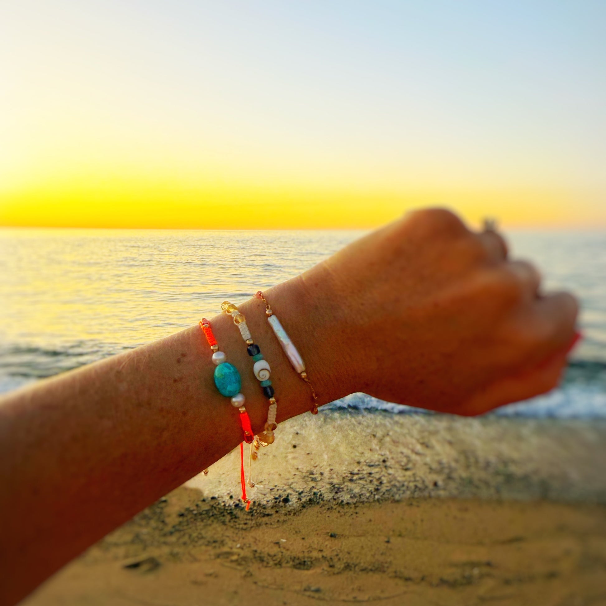 Hand with colorful bracelets on a beach at sunset