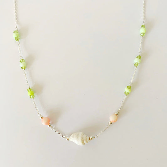 the margarita shellebration necklace by mermaids and madeleines is a station style necklace with a shell and coral beads at the center and stations of green opal and peridot spread out throughout the sterling silver chain to the clasp. this necklace is photographed on a white surface
