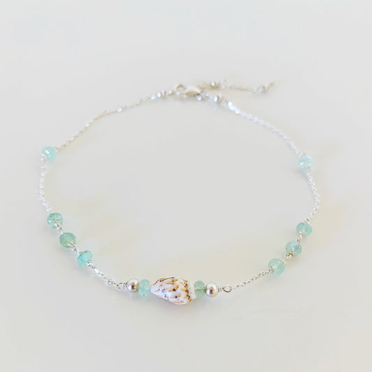 shell yeah mermaids and madeleines anklet is designed with dainty sterling chain with a shell at the center and green amethyst on the sides. this anklet is photographed on a white surface